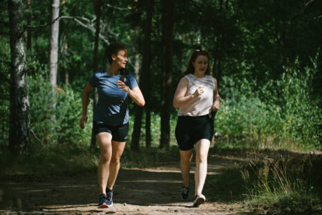 Kaksi ihmistä juoksee metsäisellä polulla tai tiellä