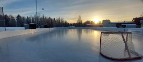 Jokelan urheilukentän ulkojääkaukalo auringon laskiessa.