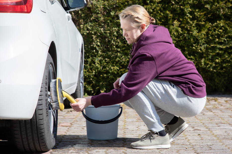 Henkilö pesee autoa kotipihassa