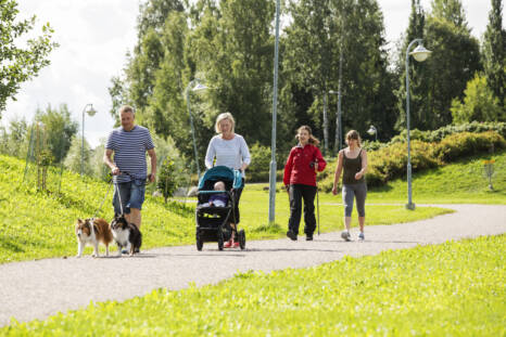 Neljä ihmistä kävelee puistossa, yksi työntää lastenrattaita
