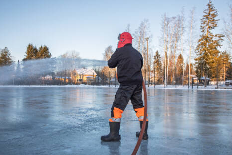 A person freezes outdoor ice with a hose in their hand.