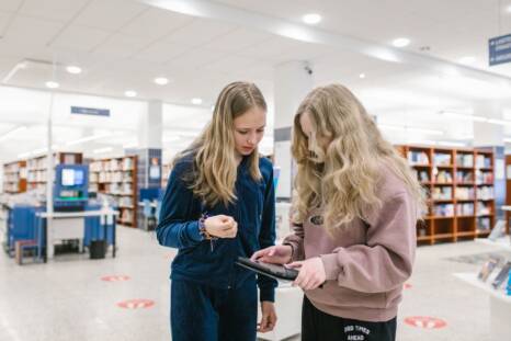 Kaksi nuorta kirjastolla tutkimassa tablettia.