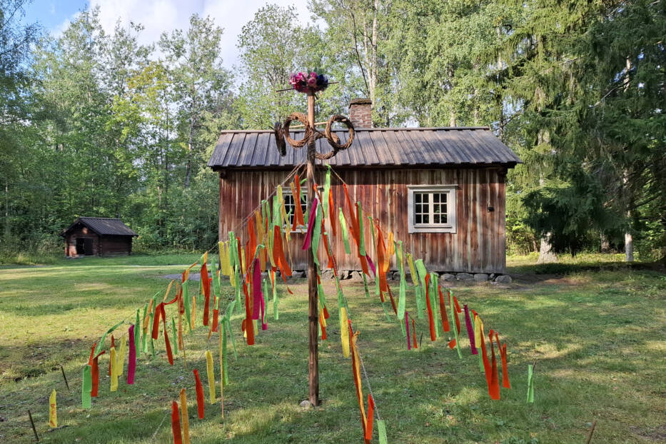 Mökin edessä runosalko, jossa värikkäitä kankaanpaloja roikkuu naruista